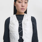 Front closeup view of snow white breno vest on model wearing black dress, against a white background.