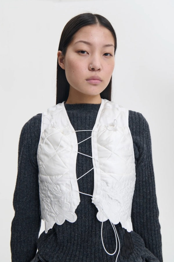 Front closeup view of snow white breno vest on model wearing black dress, against a white background.