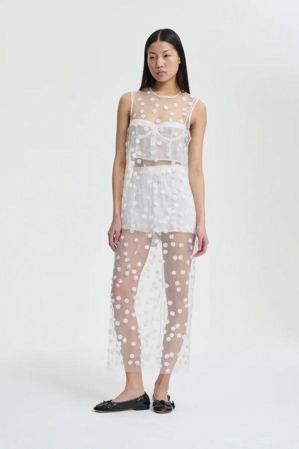 Front view of white utania top on model wearing white shorts and black flats, against a white backgound.