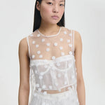 Alternate front view of white utania top on model wearing white brassiere and shorts, against a white background.