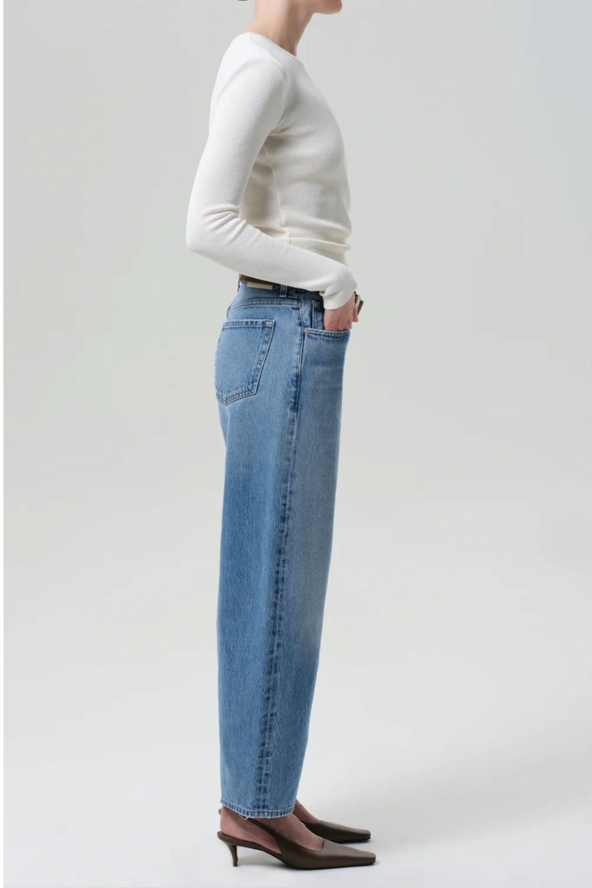 Side view of miro jean in corrin on model wearing a white t-shirt and brown heels. against a white background.