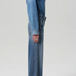 Side view of boardwalk trouser in jete on model wearing jean shirt and black heels against a white background.