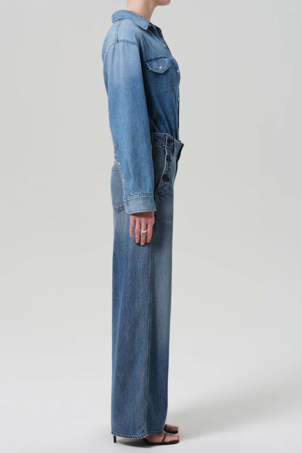 Side view of boardwalk trouser in jete on model wearing jean shirt and black heels against a white background.