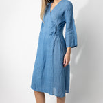 Front slanted view of denim wrap dress on barefoot model, against a white background.