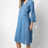 Front slanted view of denim wrap dress on barefoot model, against a white background.