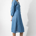 Side view of denim wrap dress on barefoot model, against a white bakground.