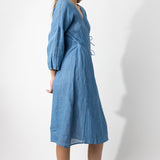 Side view of denim wrap dress on barefoot model, against a white bakground.