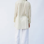 Back view of kora little subhash shirt on model wearing white pants and natural sandals, against a white background.