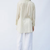 Back view of kora little subhash shirt on model wearing white pants and natural sandals, against a white background.