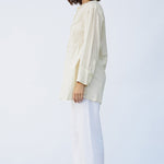 Side view of kora little subhash shirt on model wearing white pants and natural sandals, against a white background.