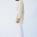 Side view of kora little subhash shirt on model wearing white pants and natural sandals, against a white background.