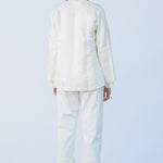Back view of rice mandarin jacket on model wearing rice pants and natural sandals, against a white background.