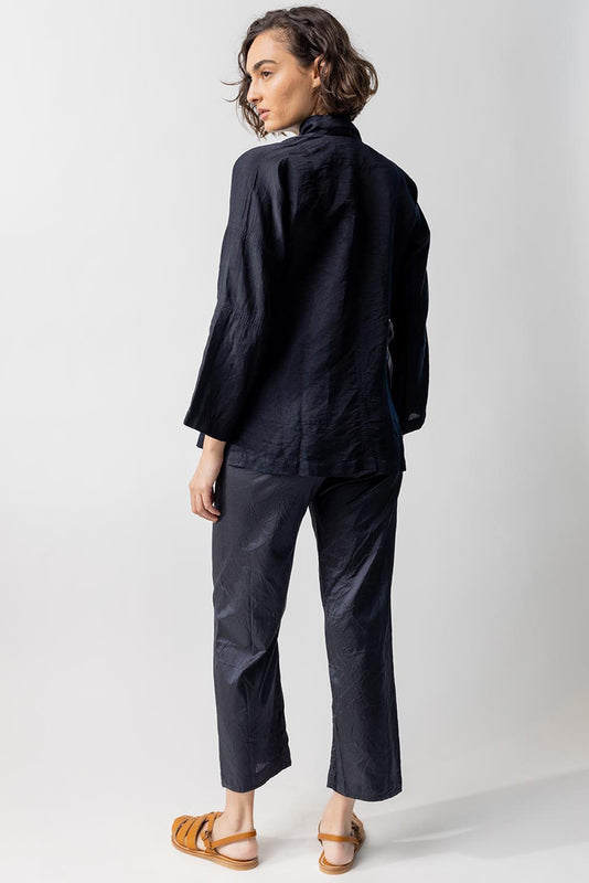 Back view of midnight mandarin jacket on model wearing midnight pants and natural sandals, against a white background.