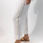 Side closeup view of pants with velvet ribbon on model wearing rice top and natural sandals, against a white background.