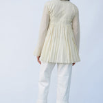 Back view of kora rabari jacket on model wearing white pants and natural sandals, against a white background.