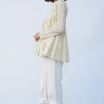 Side view of kora rabari jacket on model wearing white pants and natural sandals, against a white background.