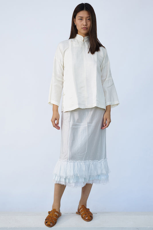 Front view of tint ruffle skirt on model wearing mandarin jacket and natural sandals, against white background.