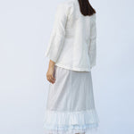 Back view of tint ruffle skirt on model wearing mandarin jacket and natural sandals, against a white background.