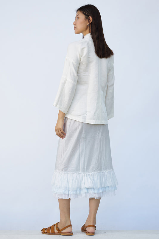 Back view of tint ruffle skirt on model wearing mandarin jacket and natural sandals, against a white background.