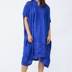 Front view of cobalt yoruba tunic on model wearing natural sandals, against a white background.