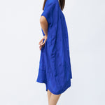 Side view of cobalt yoruba tunic on model wearing natural sandals, against a white background.