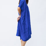 Side view of cobalt yoruba tunic on model wearing natural sandals, against a white background.