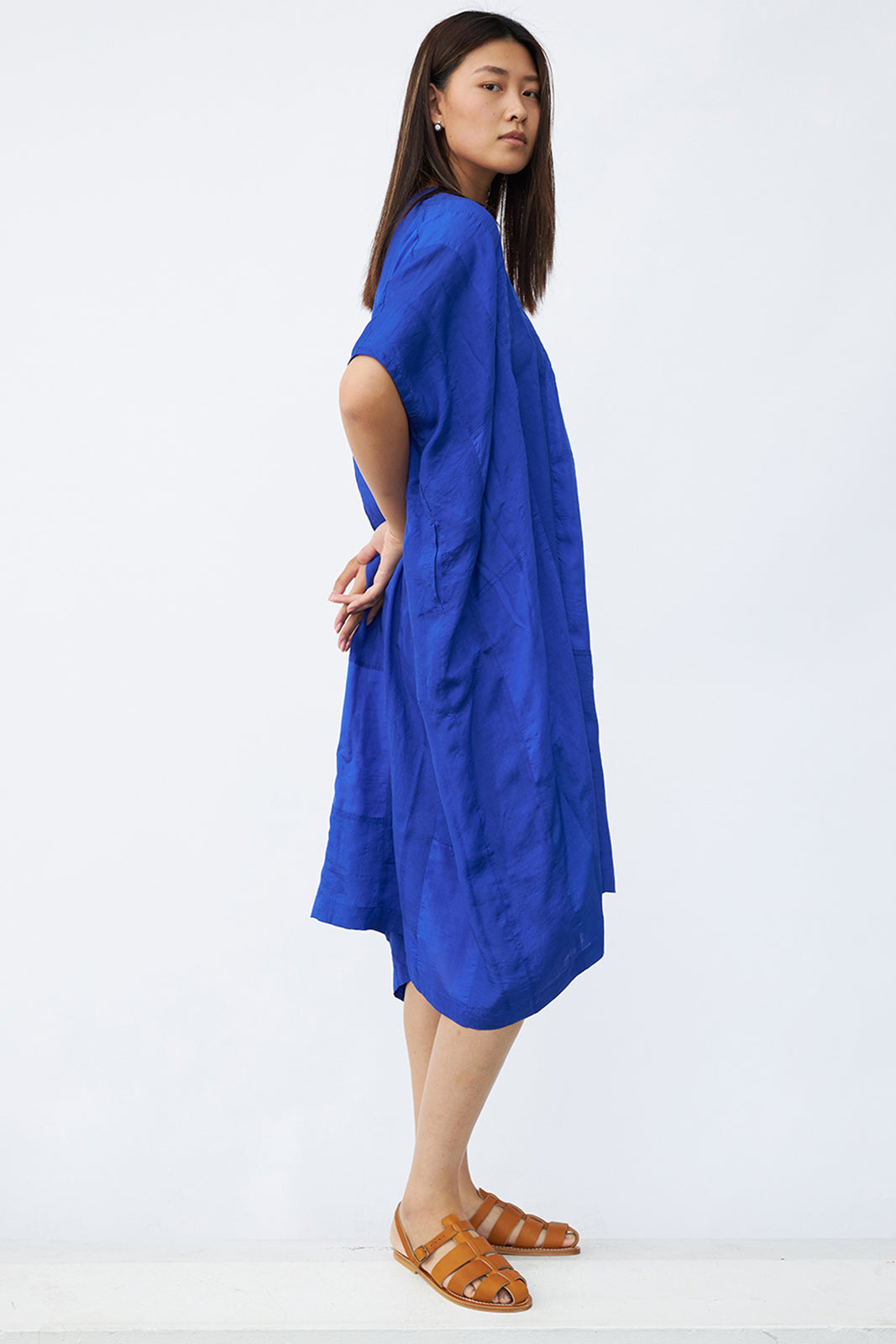 Side view of cobalt yoruba tunic on model wearing natural sandals, against a white background.