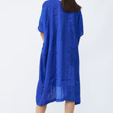 Back view of cobalt yoruba tunic on model wearing natural sandals against a white background.