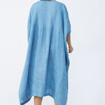 Back view of denim yoruba tunic on model wearing leather sandals, against a white background