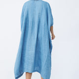 Back view of denim yoruba tunic on model wearing leather sandals, against a white background