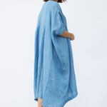 Back view of denim yoruba tunic on model wearing leather sandals, against a white background.