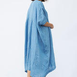 Back view of denim yoruba tunic on model wearing leather sandals, against a white background.