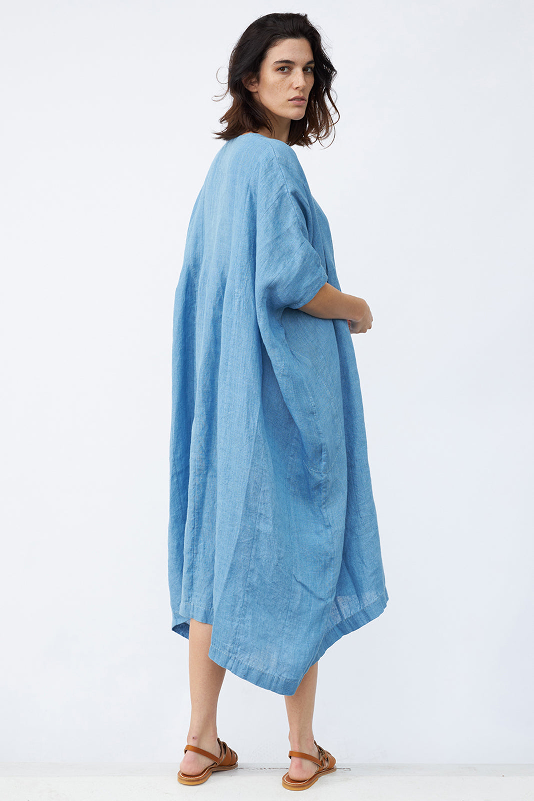 Back view of denim yoruba tunic on model wearing leather sandals, against a white background.