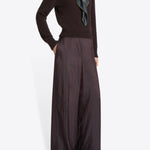 Side view of burgundy penn wide leg pant on model wearing brown sweater and floral scarf against a white background.