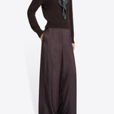 Side view of burgundy penn wide leg pant on model wearing brown sweater and floral scarf against a white background.