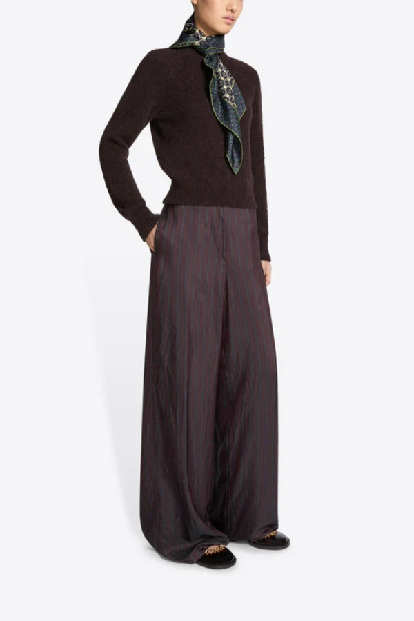 Side view of burgundy penn wide leg pant on model wearing brown sweater and floral scarf against a white background.