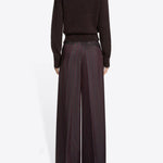 Back view of burgundy penn wide leg pant n model wearing brown sweater and floral scarf, against a white background.