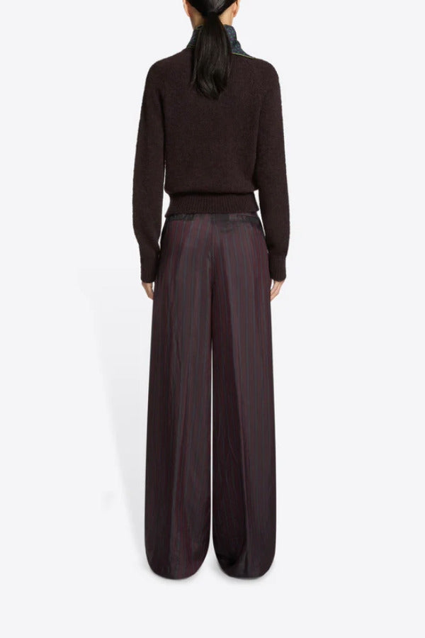 Back view of burgundy penn wide leg pant n model wearing brown sweater and floral scarf, against a white background.