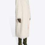 Side view of white Rivla Fringed Coat on model wearing green print boots, against a white background.