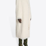 Side view of white Rivla Fringed Coat on model wearing green print boots, against a white background.