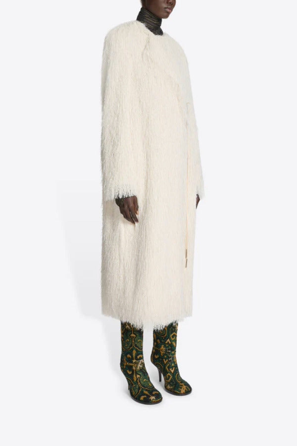 Side view of white Rivla Fringed Coat on model wearing green print boots, against a white background.