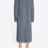 Back view of dark grey Rivla Fringed Coat on model wearing white heels, against a white background.