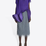 Front view of dark grey sonka tris fringed skirt on model wearing purple top with white heels, against a white background.