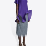 Side view of dark grey sonka tris fringed skirt on model wearing purple top and white heels, against a white background.