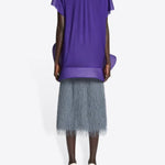 Back view of dark grey sonka tris fringed skirt on model wearing purple top and white heels, against a white background.