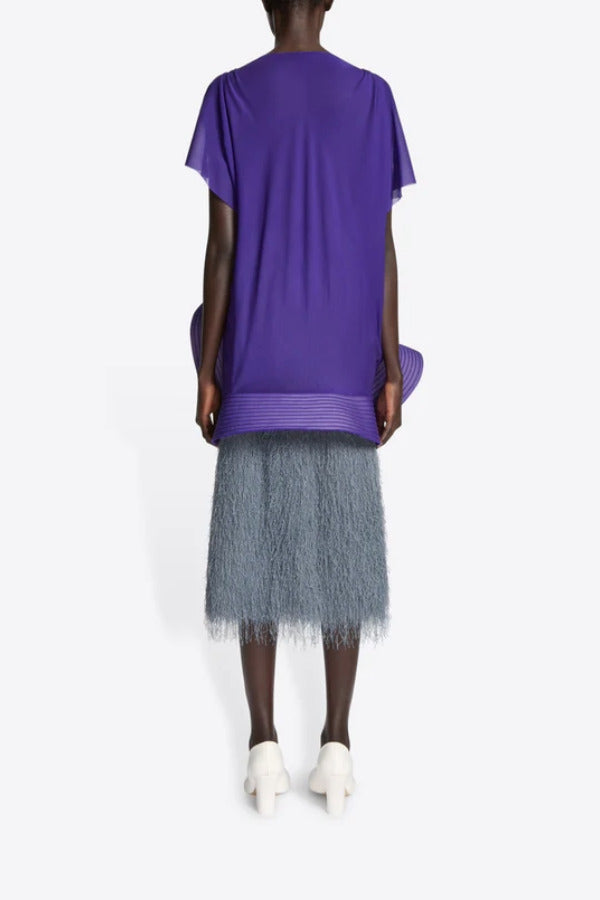 Back view of dark grey sonka tris fringed skirt on model wearing purple top and white heels, against a white background.