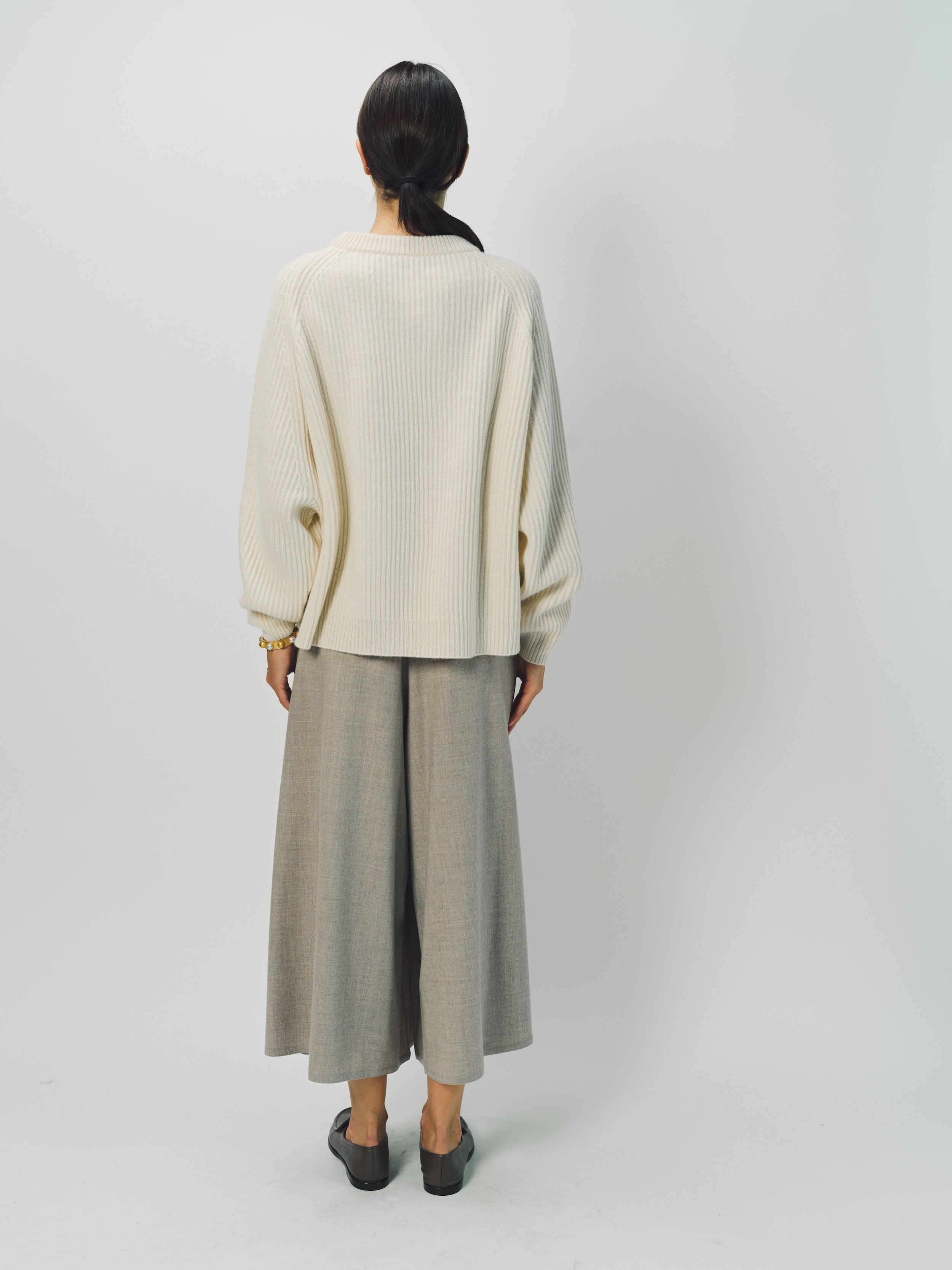 Back view of bone ls crew neck sweater on model wearing grey pants, against a white background.