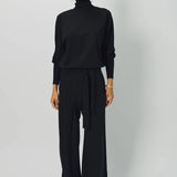 Front view of black ls t-neck raglan sweater on model wearing black pants, against a white background. 