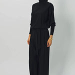 Front slanted view of black ls t-neck raglan sweater on model wearing black pants, against a white background.