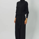 Front slanted view of black ls t-neck raglan sweater on model wearing black pants, against a white background.